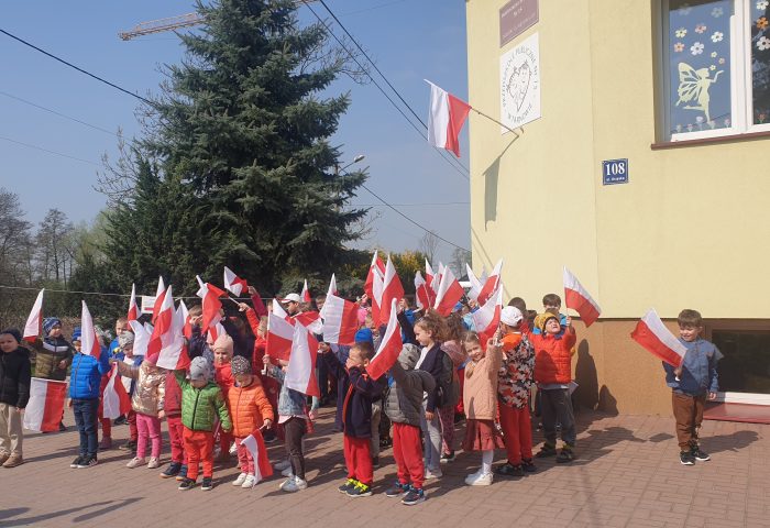 Dzieci z gr.1, 2,3 z flagą pod budynkiem przedszkola
